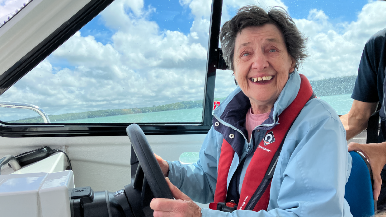 Older women driving a boat on the sea and smiling to the camera.png