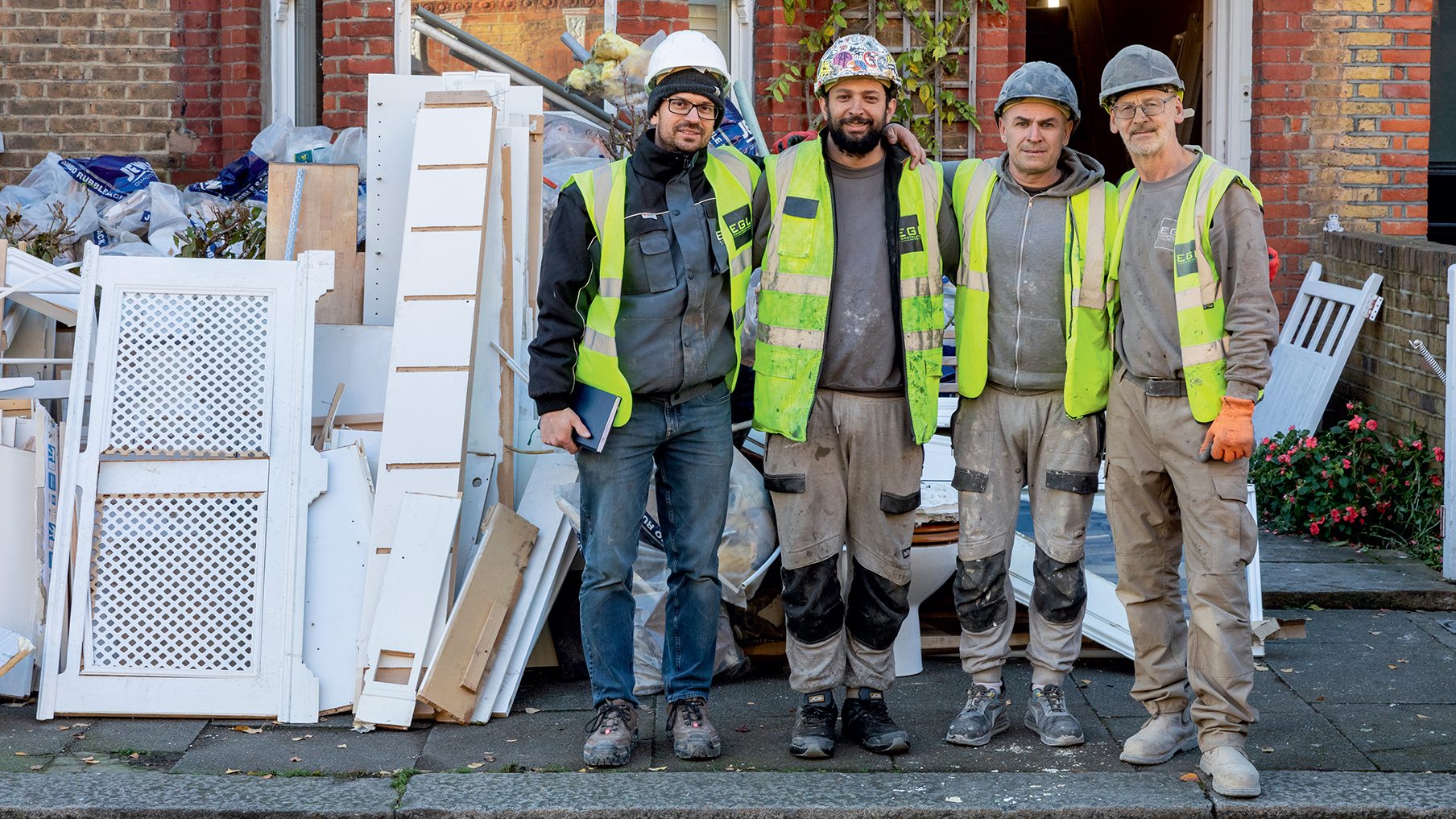four-deaf-builders-wearing-hard-hats-hi-vis-jackets-and-plain-clothes-pose-outside-a-home-construction-site.jpg