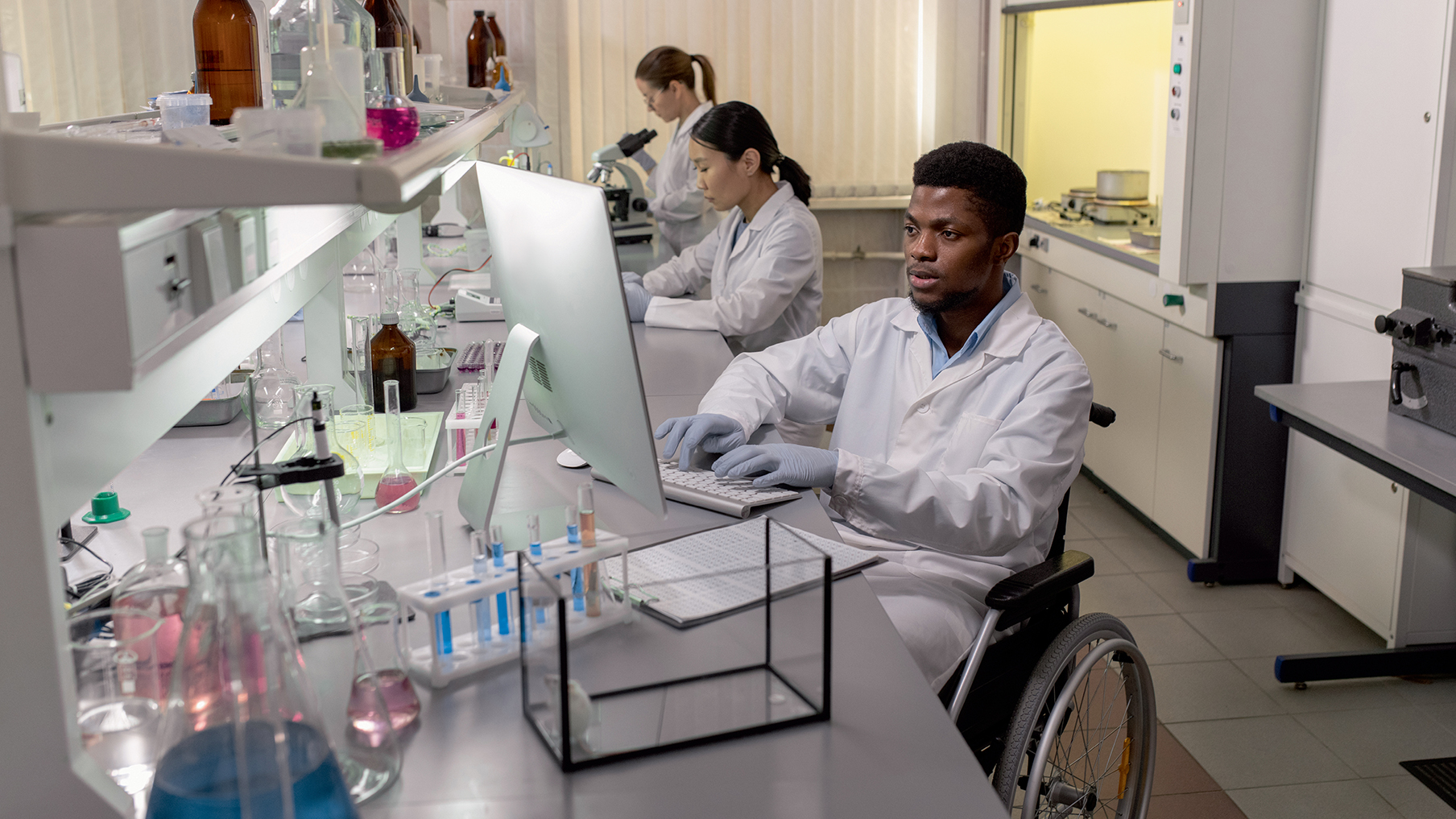 A photo of a lab with scientists working, one being a wheelchair user
