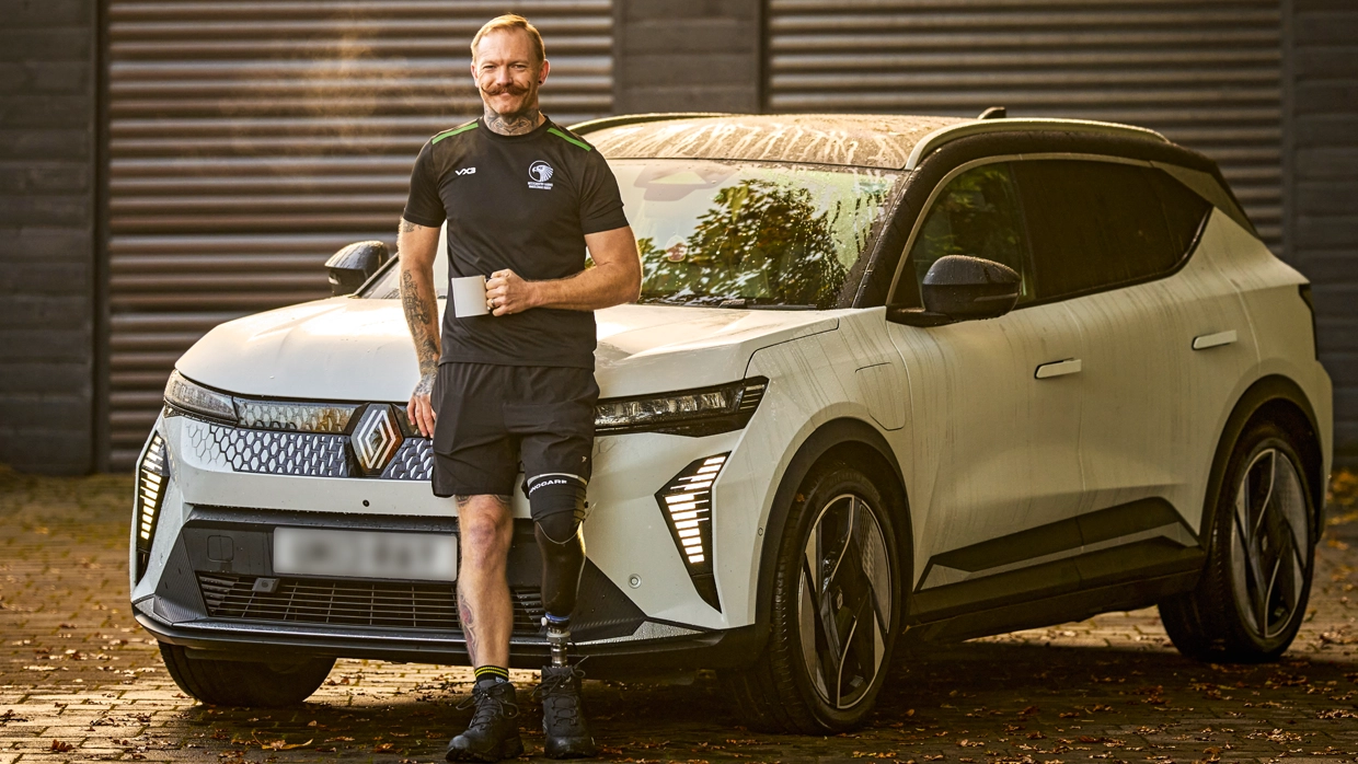A photo of Ray holding a mug outside standing in front of his car 
