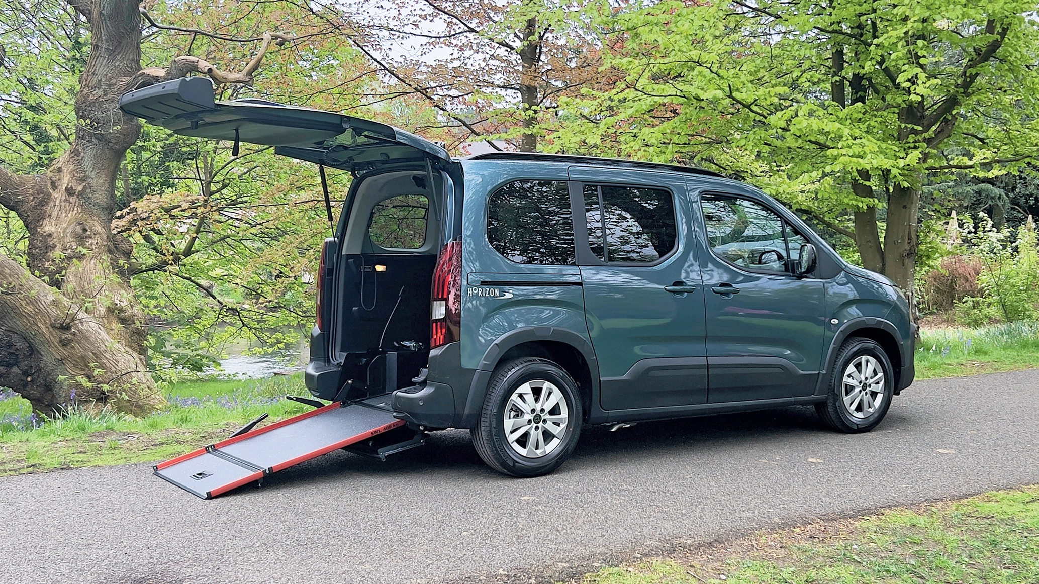 An image of a Peugeot Rifter WAV, parked in a woodland area with its tailgate open